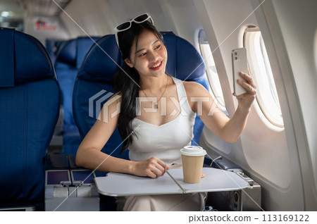 An attractive Asian female passenger is taking a selfie with her smartphone during the flight. An attractive Asian female passenger is taking a selfie with her smartphone during the flight. 113169122