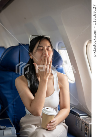 A female passenger is feeling tired and sleepy during a long flight, while traveling by plane. 113169127