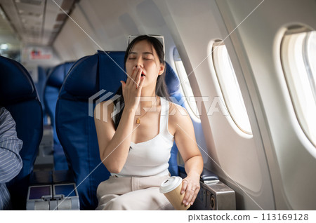 A female passenger is feeling tired and sleepy during a long flight, while traveling by plane. A female passenger is feeling tired and sleepy during a long flight, while traveling by plane. 113169128