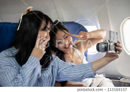Two happy Asian female passengers are taking a selfie together during the flight. 113169137