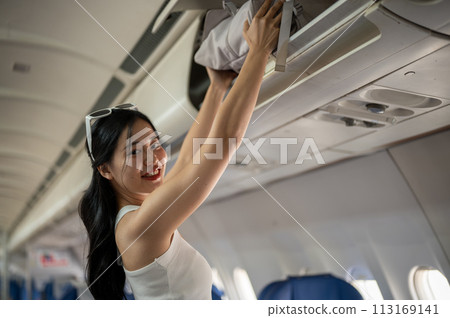 An attractive Asian female passenger is putting her bag in an overhead bin, traveling by plane. An attractive Asian female passenger is putting her bag in an overhead bin, traveling by plane. 113169141
