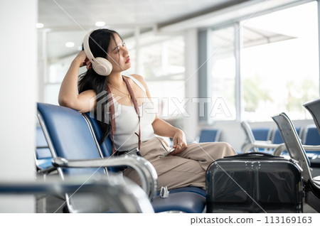 A female passenger is waiting for her boarding call in the airport terminal, looking at the runway. 113169163