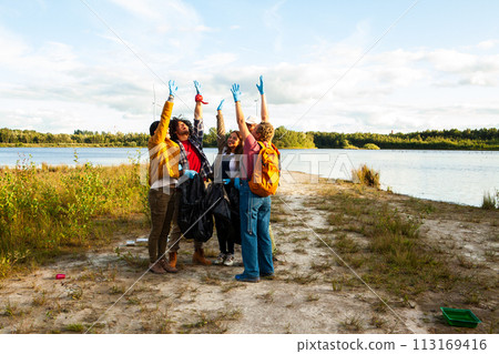 Volunteer Team Jubilantly Raises Hands After Shoreline Cleanup 113169416