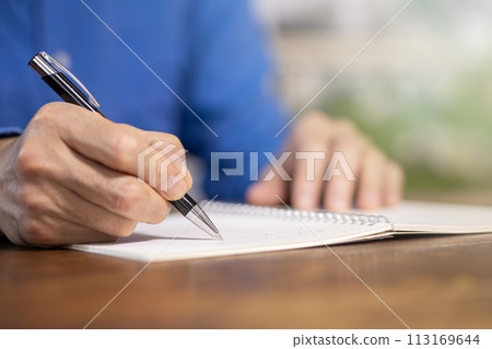 一個人用原子筆在木桌上的筆記本上寫字 113169644