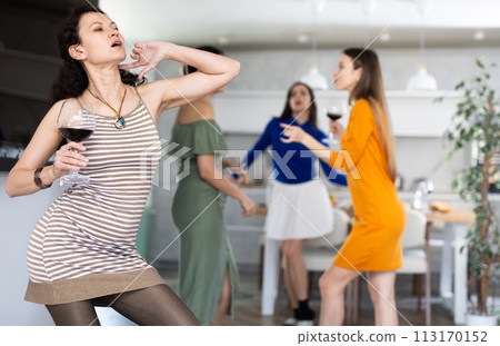 Cheerful woman dancing with wine glass at friendly house party 113170152