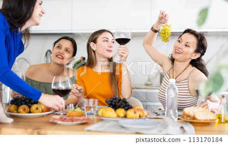 Girlfriends chatting and drinking wine in kitchen 113170184