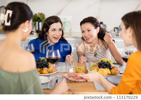Girlfriends chatting and drinking wine in kitchen 113170229