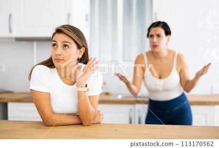 Woman listening her girlfriend standing behind and quarreling with her Woman listening her girlfriend standing behind and quarreling with her 113170562
