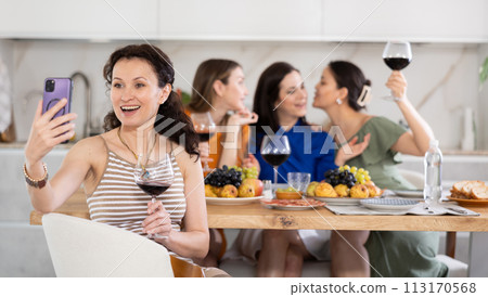 Caucasian smiling girl is sitting on chair and taking selfies during gatherings with friends Caucasian smiling girl is sitting on chair and taking selfies during gatherings with friends 113170568