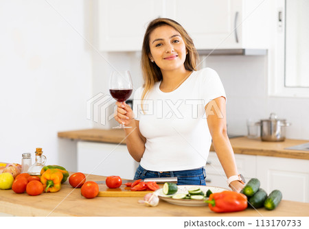 Cheerful young Hispanic woman enjoying wine while preparing dinner Cheerful young Hispanic woman enjoying wine while preparing dinner 113170733