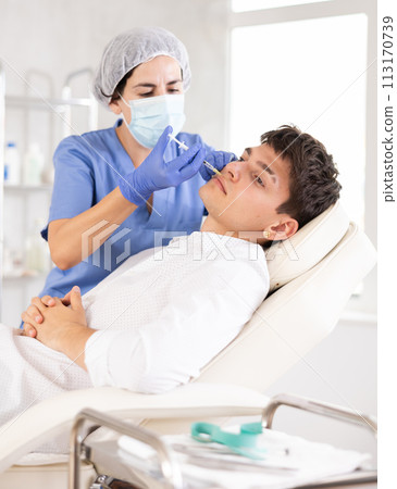 Young man having face care by means of injection in aesthetic clinic Young man having face care by means of injection in aesthetic clinic 113170739
