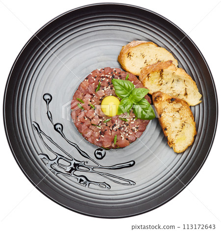 Tuna and avocado tartare with sesame seeds, capers and egg yolk on a dark ceramic plate with baguette bread crouton chips 113172643