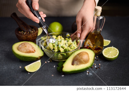 Woman mixing Sliced chopped avocado fruit with lime juice and species in a glass bowl at domestic kitchen Woman mixing Sliced chopped avocado fruit with lime juice and species in a glass bowl at domestic kitchen 113172644