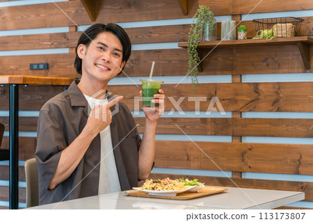 Young man drinking green smoothie while eating lunch at a cafe (enzyme/detox/dietary fiber/health food) 113173807