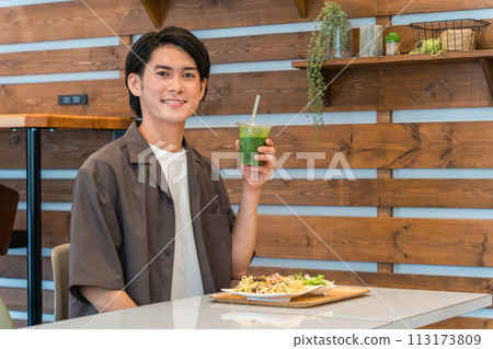 Young man drinking green smoothie while eating lunch at a cafe (enzyme/detox/dietary fiber/health food) Young man drinking green smoothie while eating lunch at a cafe (enzyme/detox/dietary fiber/health food) 113173809