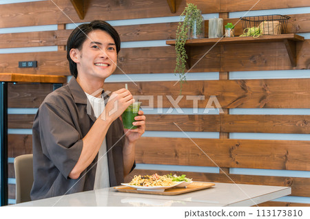 Young man drinking green smoothie while eating lunch at a cafe (enzyme/detox/dietary fiber/health food) Young man drinking green smoothie while eating lunch at a cafe (enzyme/detox/dietary fiber/health food) 113173810