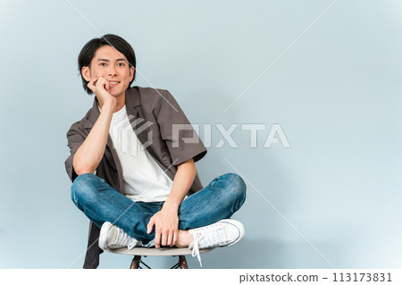 一個穿著運動鞋和牛仔褲的清爽男人坐在椅子上 113173831
