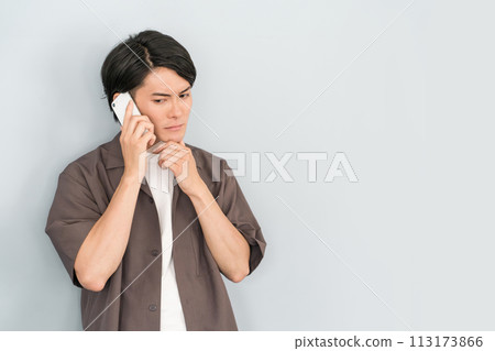 年輕的亞洲男子在智慧型手機上說話/打電話（可疑/可疑/預約電話/詐騙/可疑電話/滋擾電話） 113173866
