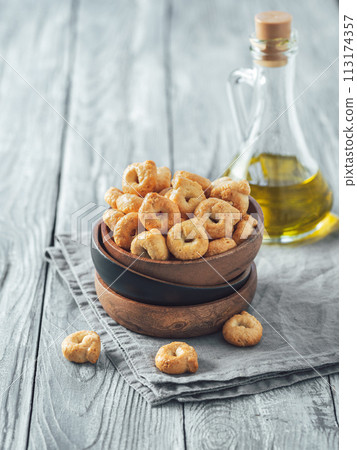 Traditional italian snack taralli or tarallini in wooden bowl over old gray wooden table. Rustic shot of taralli appetizer with copy space. Vertical. Traditional italian snack taralli or tarallini in wooden bowl over old gray wooden table. Rustic shot of taralli appetizer with copy space. Vertical. 113174357