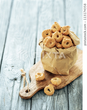 Traditional italian snack taralli or tarallini in paper bag over old gray wooden table. Rustic shot of taralli appetizer with copy space 113174358
