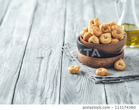 Traditional italian snack taralli or tarallini in wooden bowl over old gray wooden table. Rustic shot of taralli appetizer with copy space 113174360