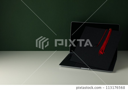 A graduate's hat on a laptop, on a green background. 113176568