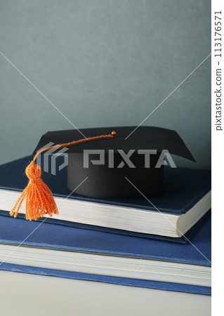 Graduation hat with books on a table on a dark background. 113176571