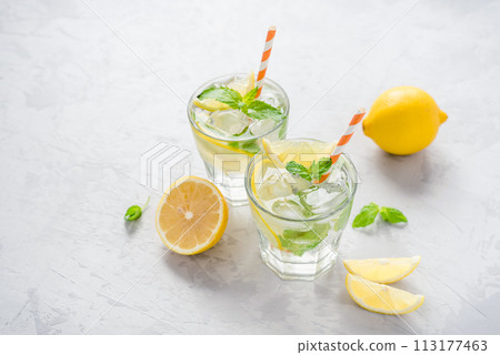 Two glasses of lemonade adorned with ice, lemon slices, and fresh mint leaves. 113177463