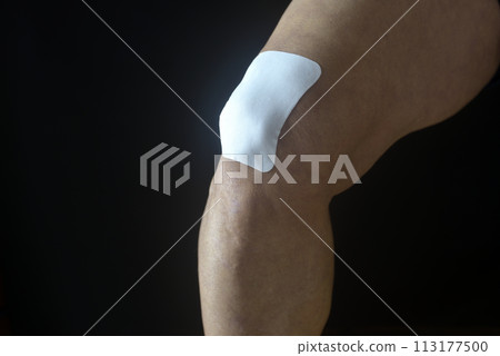 將藥膏塗在一位患有膝蓋疼痛的老人的膝蓋上 將藥膏塗在一位患有膝蓋疼痛的老人的膝蓋上 113177500