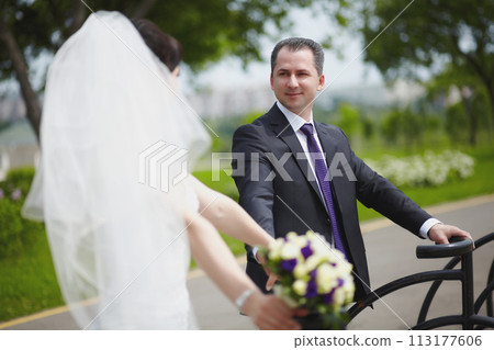 The bride and groom pose by the road in the park on a summer day The bride and groom pose by the road in the park on a summer day 113177606