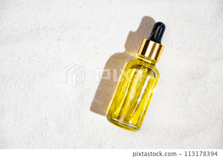 Natural cosmetic oil in a glass jar with a pipette on the sand, top view, copy space for text 113178394