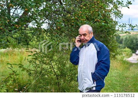 Elderly retired man walking talking on the phone in a august september garden Elderly retired man walking talking on the phone in a august september garden 113178512