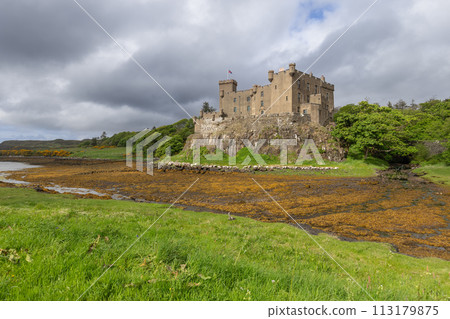 Dunvegan Castle with stone walls overlooks vibrant algae shoreline on Isle of Skye under dynamic sky Dunvegan Castle with stone walls overlooks vibrant algae shoreline on Isle of Skye under dynamic sky 113179875