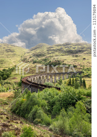 Glenfinnan Viaduct ancient stones arc over vibrant natural tapestry in Scotland under vast clouds 113179894
