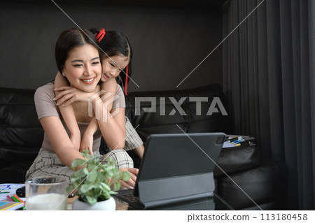 Cute little girl hugging her mother from the back, sitting on couch at home 113180458