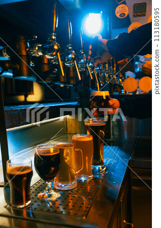 Craft beer tap pouring frothy beverage with range of filled light and dark beer, ale glasses in front. Serving craft beer from tap. Craft beer tap pouring frothy beverage with range of filled light and dark beer, ale glasses in front. Serving craft beer from tap. 113180595