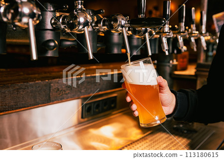 Bartender pouring light, cold foamy beer from tap into glass at bar with multiple beer dispensers. Serving craft beer from tap. Oktoberfest concept. 113180615