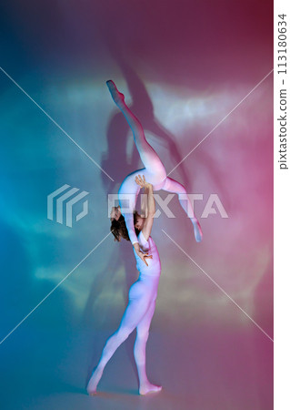 Male ballet dancer supporting female dancer in challenging, artistic lift pose in neon light against gradient studio background. 113180634