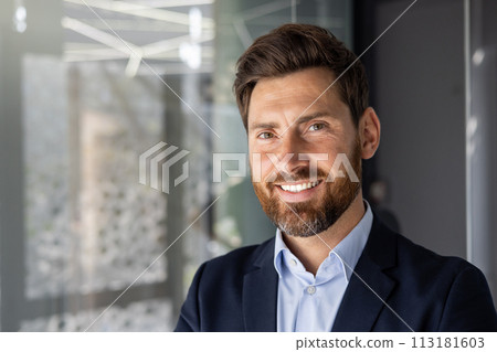 A professional portrait of a smiling businessman with a beard, standing in a well-lit, contemporary office environment. A professional portrait of a smiling businessman with a beard, standing in a well-lit, contemporary office environment. 113181603