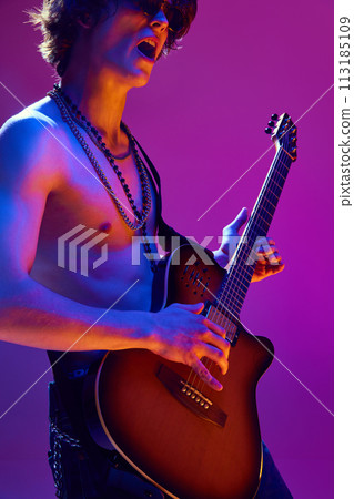 Talented and artistic young man, shirtless musician playing electric guitar against pink background in neon light Talented and artistic young man, shirtless musician playing electric guitar against pink background in neon light 113185109