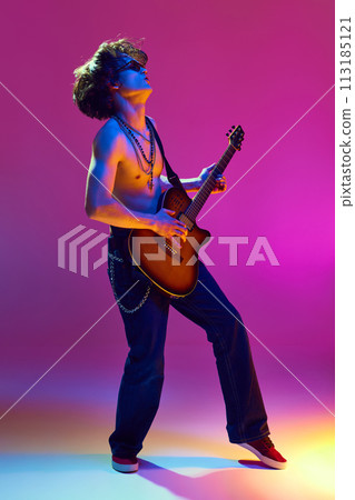 Rock and roll concert. Artistic and emotional shirtless young man playing guitar against pink background in neon light 113185121