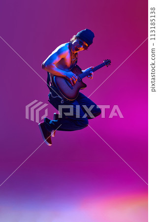Energetic young shirtless man in sunglasses,rocket playing guitar against pink background in neon light 113185138