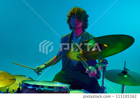 Rock band live concert. Young man in stylish clothes, musician playing drums against blue background in neon light 113185162