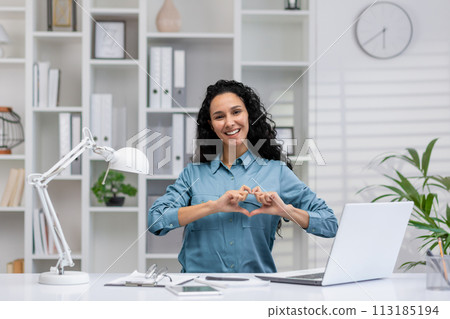 Professional Hispanic woman at home office making heart gesture, expressing love and passion for her job. 113185194