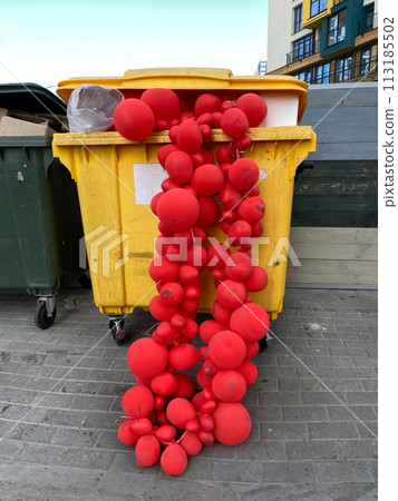 Red balloon garlands in a dumpster. Discarded used decoration. Concept of the melancholy after holiday party 113185502