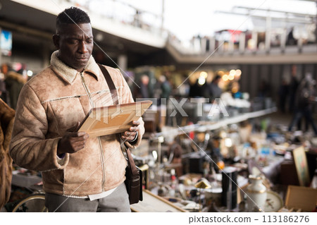 ordinary Afro-American guy considers things sacond hands on flea market ordinary Afro-American guy considers things sacond hands on flea market 113186276