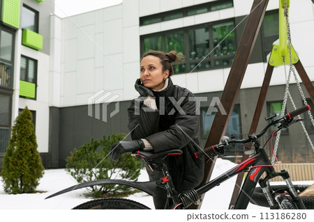 A pretty brunette woman stands with a sports bike in the yard of her house 113186280