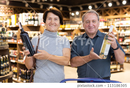 Mature couple choosing nice bottle of wine in supermarket 113186305