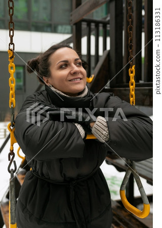 Lifestyle concept, carefree brunette woman in a black winter jacket walking on the playground 113186331