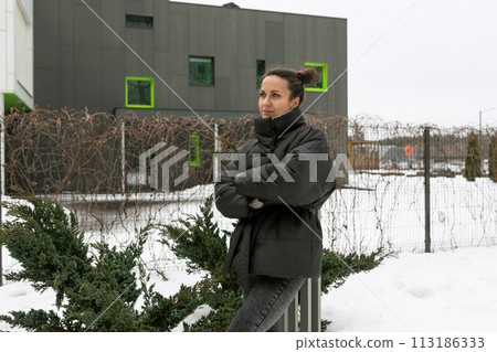 European young woman dressed in winter clothes walks in the yard 113186333